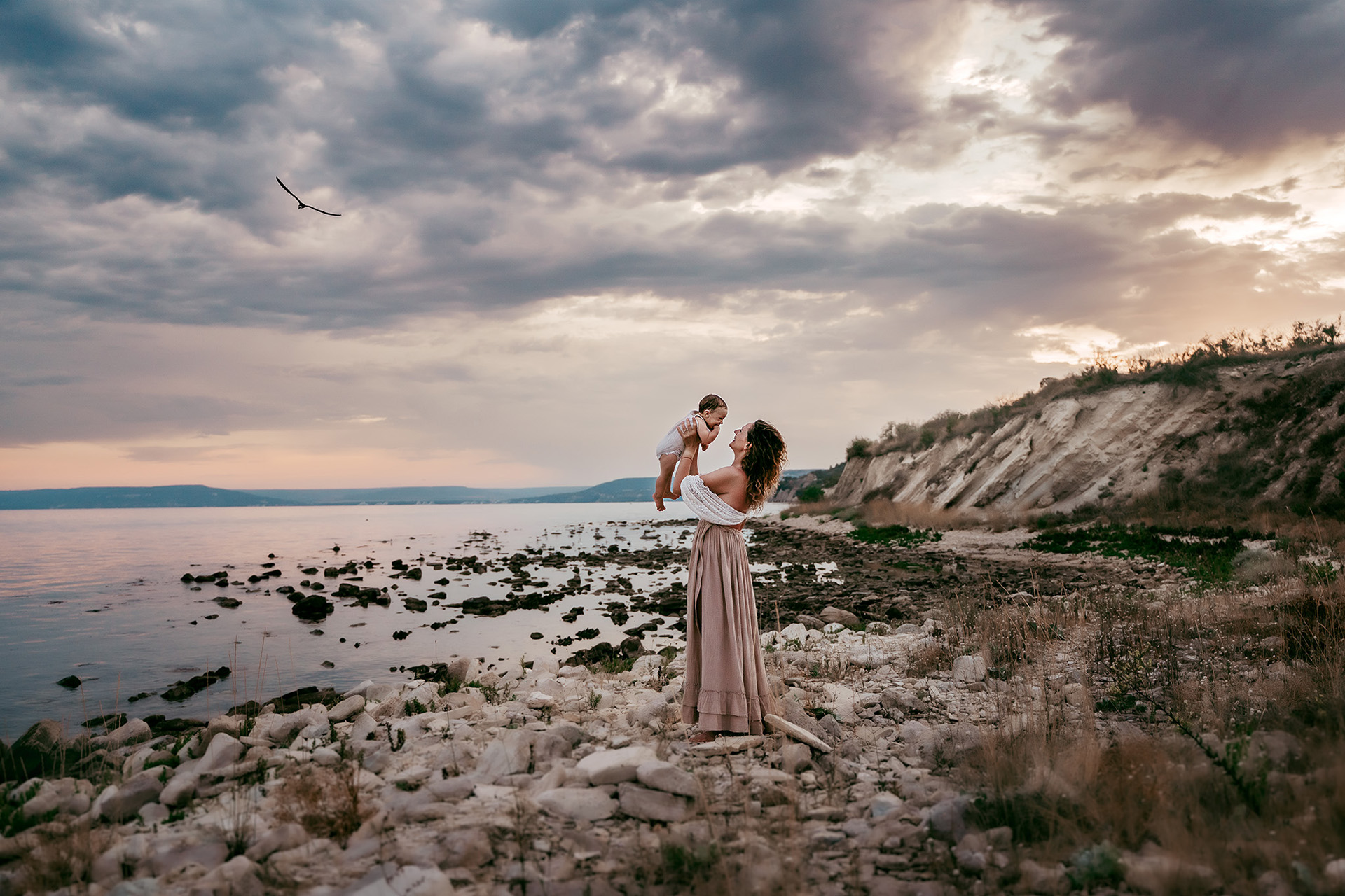 a woman holding a baby on a rocky beach